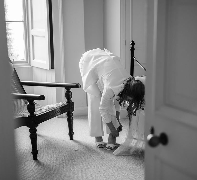 Bride puts on her shoes whilst wearing bridal suit on her wedding day