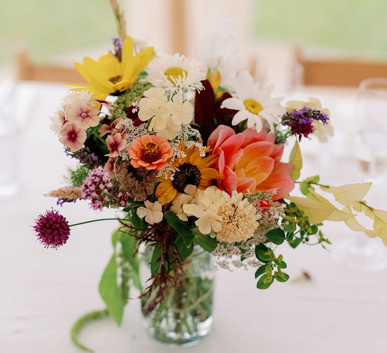 Locally grown bright florals complete with green foliage on white tablecloth 