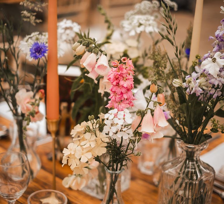 Colourful florals in vases line wooden tables surrounded by pastel candles