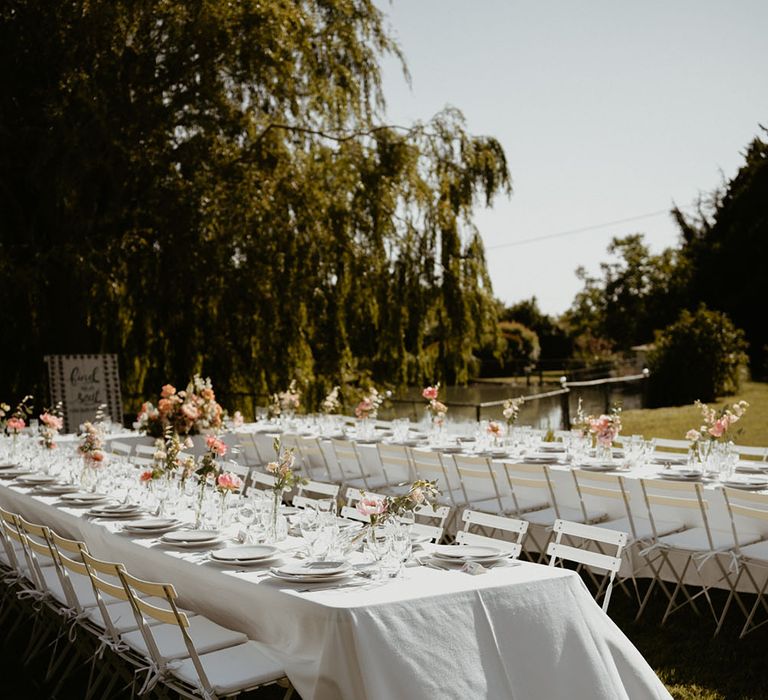 Outdoor wedding reception tables finished with white tablecloths and small pale pink floral arrangements lining the tables