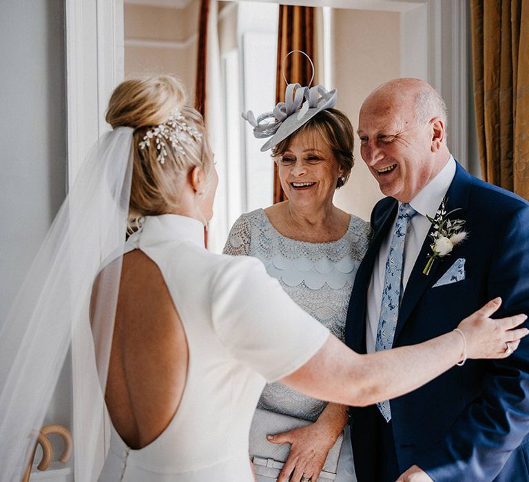 Bride in a high neck backless wedding dress greets her parents on her wedding day in blue outfits 