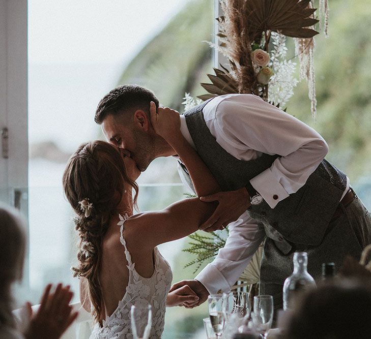 Bride & groom kiss during wedding speeches after outdoor wedding ceremony at Tunnels Beach