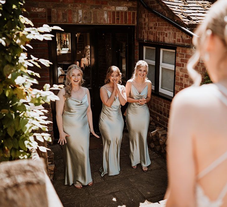 Bridesmaids wear cowl neck pale green satin bridesmaid dresses and see bride during first look moment 