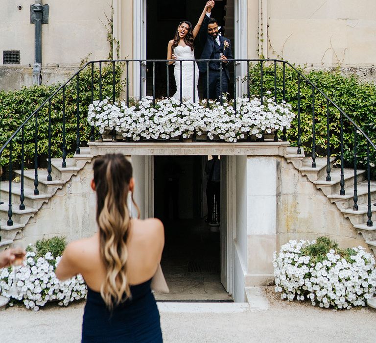 Bride & groom stand on balcony complete with white florals at Syon Park 