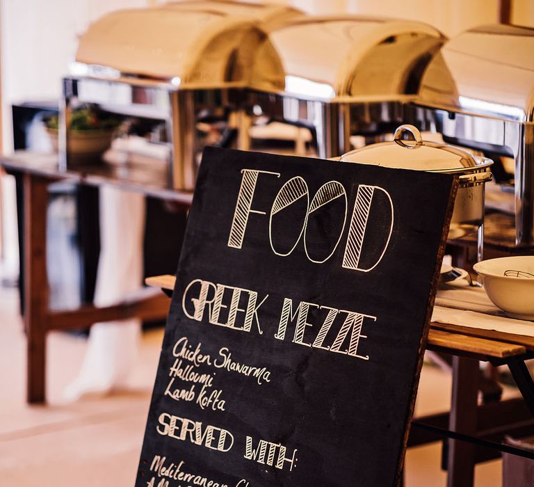 Wedding food menu on a chalkboard with the couple serving Greek food 