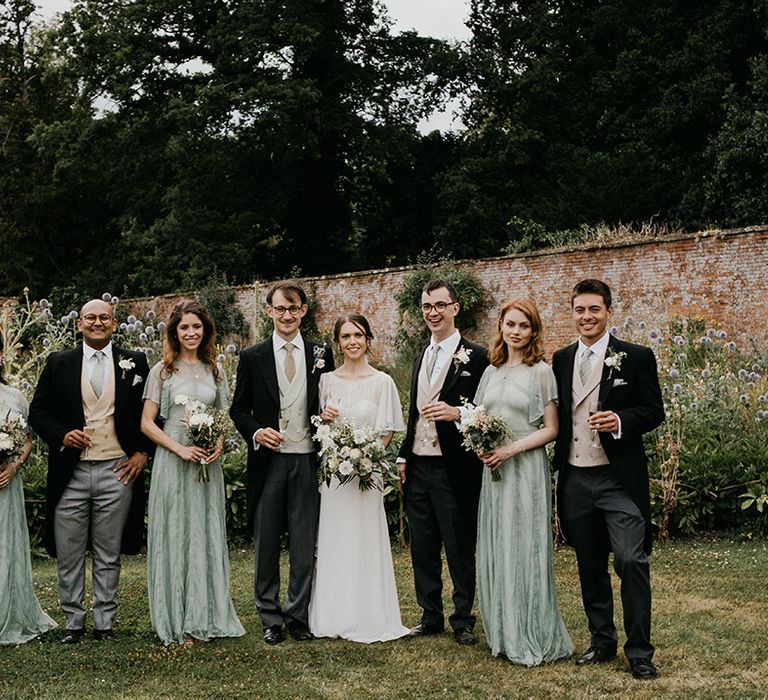 Bridesmaids in mint green long bridesmaid dresses, groomsmen in three piece suits with light waistcoats and boutonnieres with the bride and groom