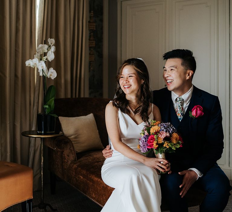 Bride holds brightly coloured floral bouquet and sits beside her groom wearing pink rose buttonhole 