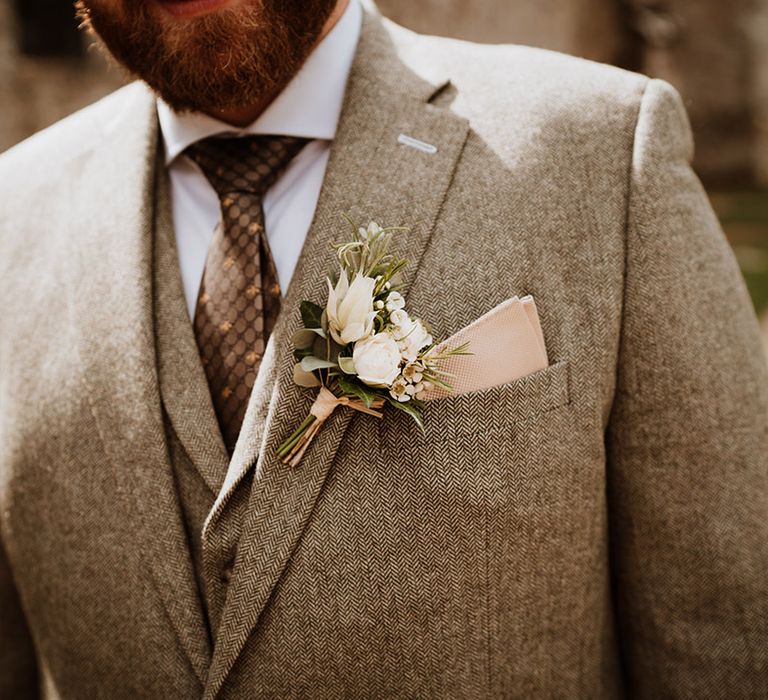 The groom in a grey tweed three piece suit with a pink pocket square and white flower buttonhole 