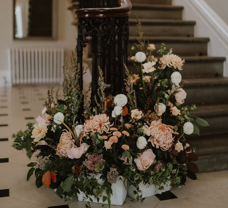 Neutral toned mixed floral arrangement decor at bottom of the stairs at St Tewdrics House, Monmouthshire 