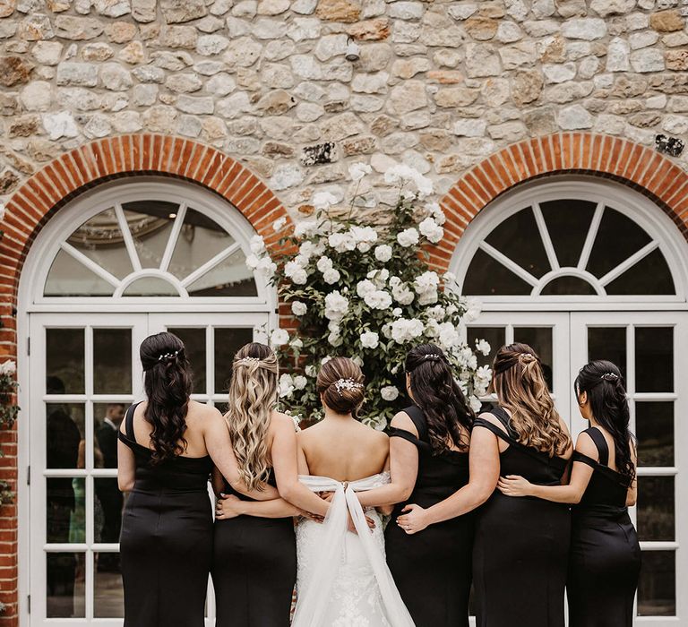 The bride in a lace wedding dresses poses with her bridesmaids in one shoulder black dresses for a traditional wedding 