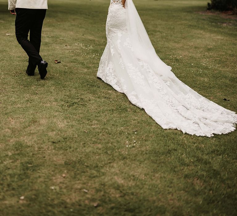 Groom in a white suit jacket walks hand in hand with the bride in an off the shoulder lace wedding dress 