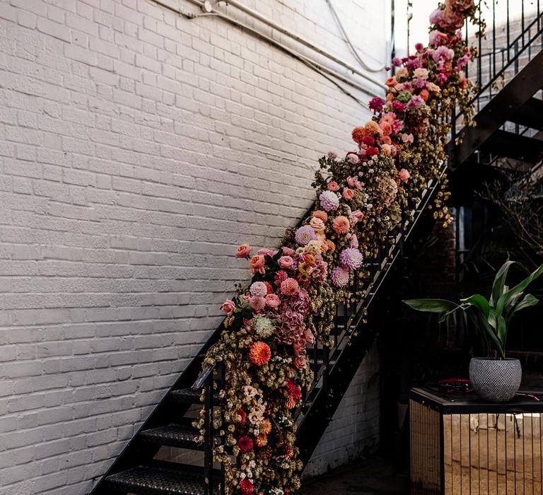 Pink, orange and purple wedding flower arrangement with dahlias decorating the banister 