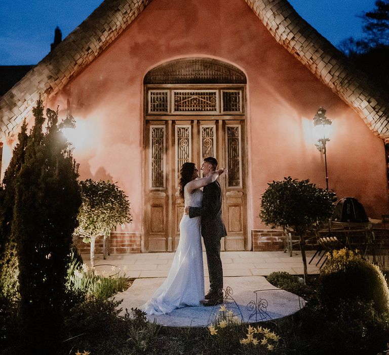 Bride & groom embrace in front of Le Petit Chateau at night surrounded by lighting 