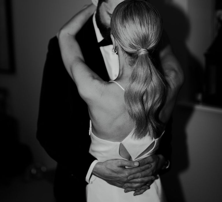 Bride wears her hair in a sleek ponytail for the wedding reception in a white dress with the groom in traditional black tux 