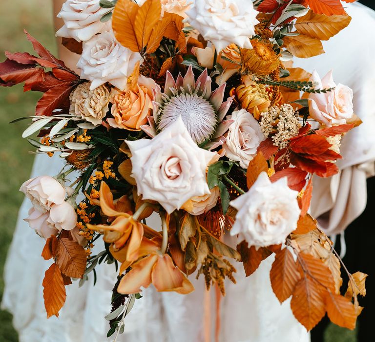 Bride holds large burnt orange bridal bouquet complete with pastel pink roses and tied with raw edge orange ribbon