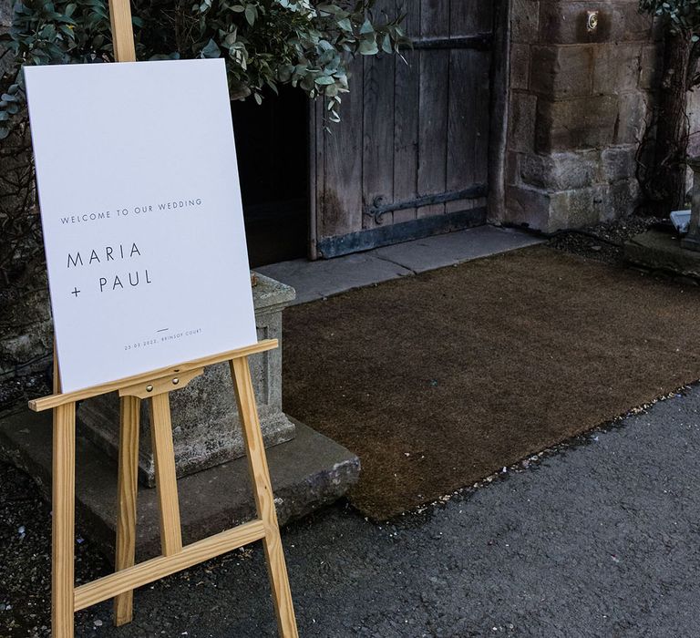 Minimal black and white wedding welcome sign on a wooden easel at the entrance to the country house wedding venue 