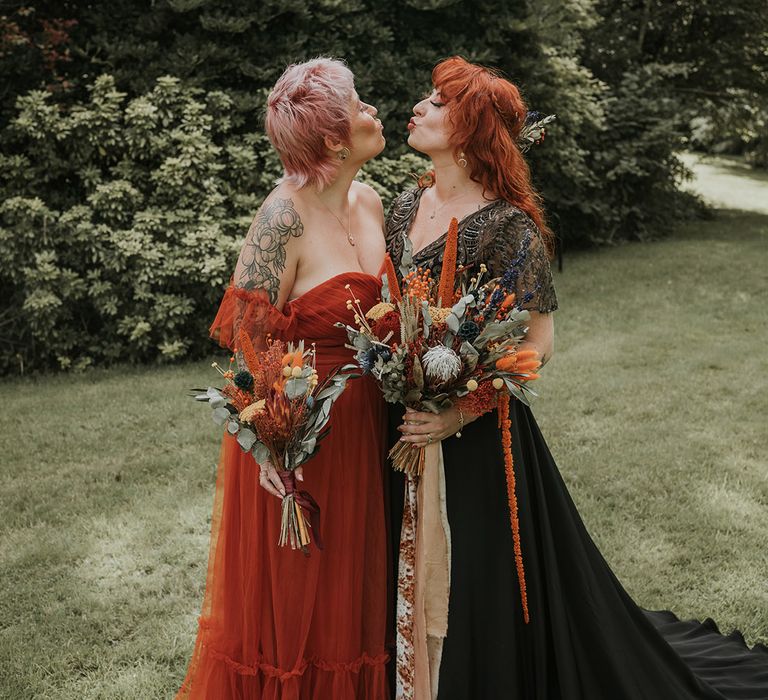 Bridesmaid in burnt orange off the shoulder bridesmaid dress and bride in black dress for wedding in Devon, both holding large dried flower wedding bouquets 