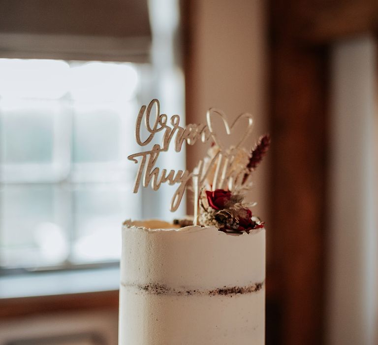 Rustic white frosted wedding cake with red rose and dried flower decor with wooden laser cut cake topper and cupcakes 