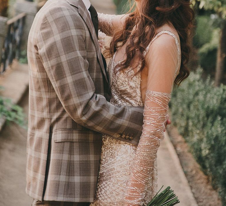 Spanish destination wedding with groom in a grey check suit embracing his bride in a bespoke sparkly wedding dress