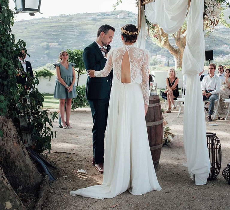 Bride and groom exchanging vows at their wooden frame altar with drapes and dried flower decor 