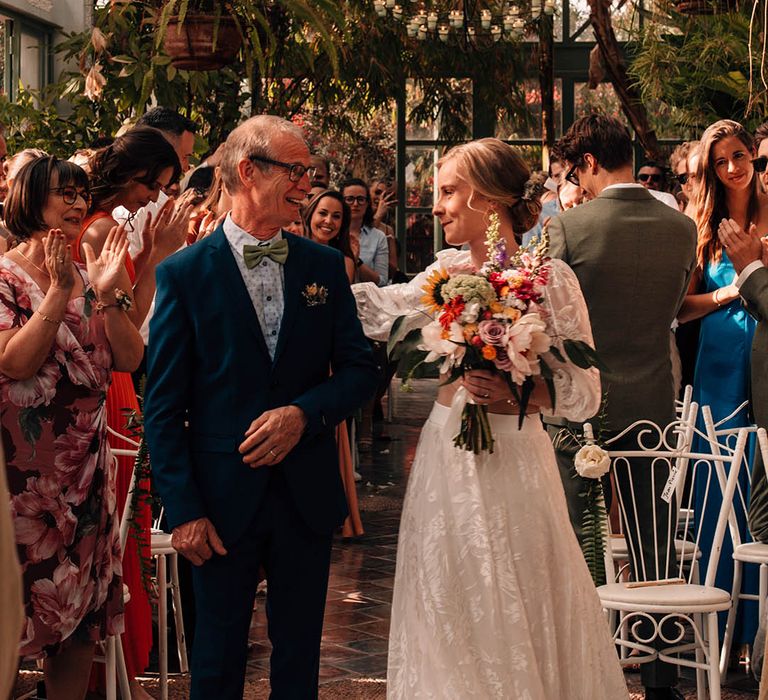 Bride in long skirt and crop top bridal separates hugging her father as she walks to the groom 