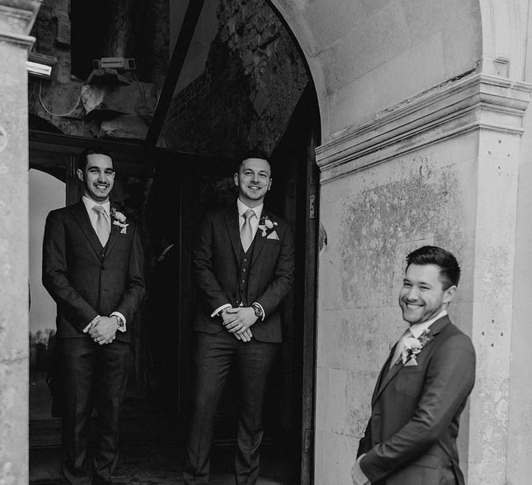 The groomsmen stand together at the entrance of Lulworth Castle to usher the guests into the venue for the ceremony 