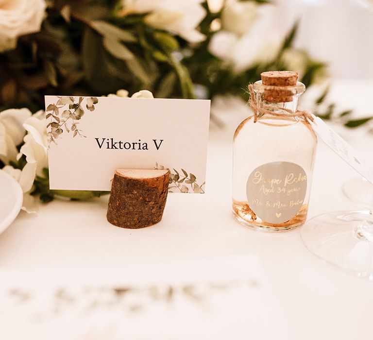 name place card in a wooden holder and small bottle wedding favour