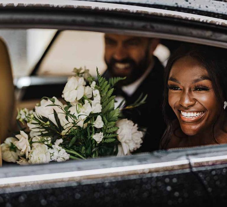 Bride holding white garden rose, white hydrangea, cows parsley and foliage bridal bouquet in classic black wedding car on her way to Lains Barn wedding reception