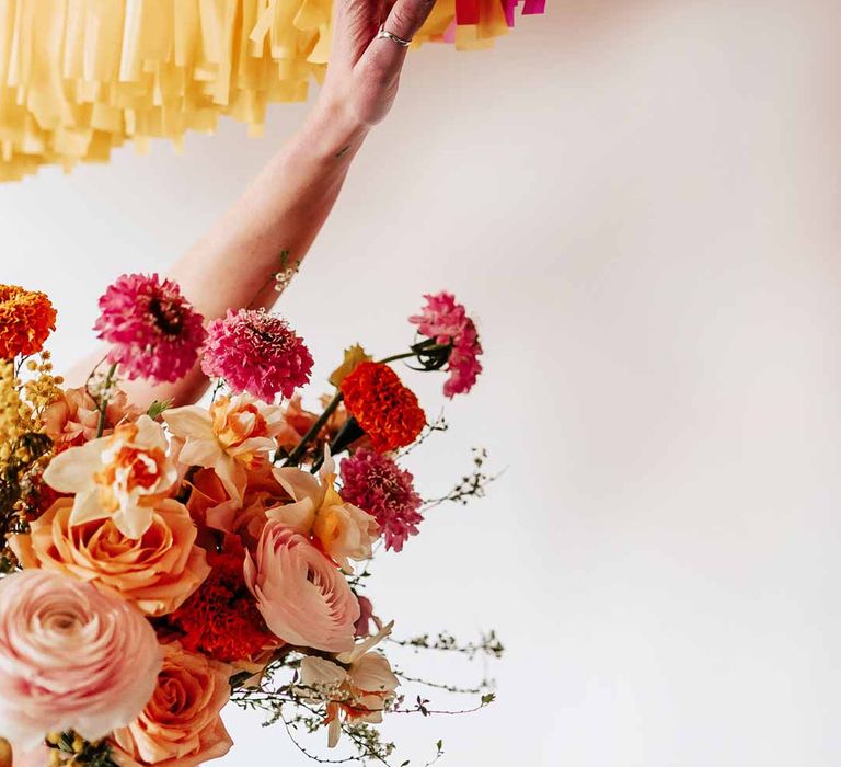 Bride with silver wedding jewellery holding colourful mixed floral bridal bouquet touching yellow and pink wedding streamers at Northern Monk Refectory Leeds