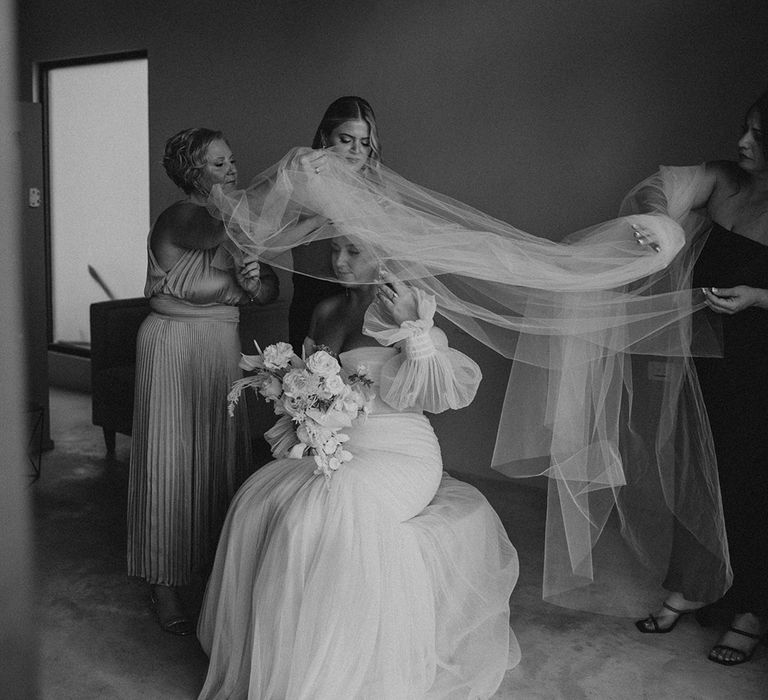 wedding morning bridal preparations with the bridal party helping the bride put on her long wedding veil 