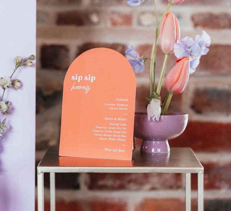 Orange semi-circle wedding sign next to lilac vase with tulips and bluebells 