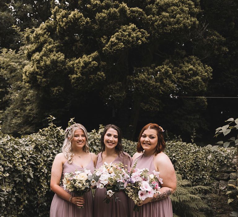 Bridesmaids in pink bridesmaid dresses holding pastel wedding bouquets 