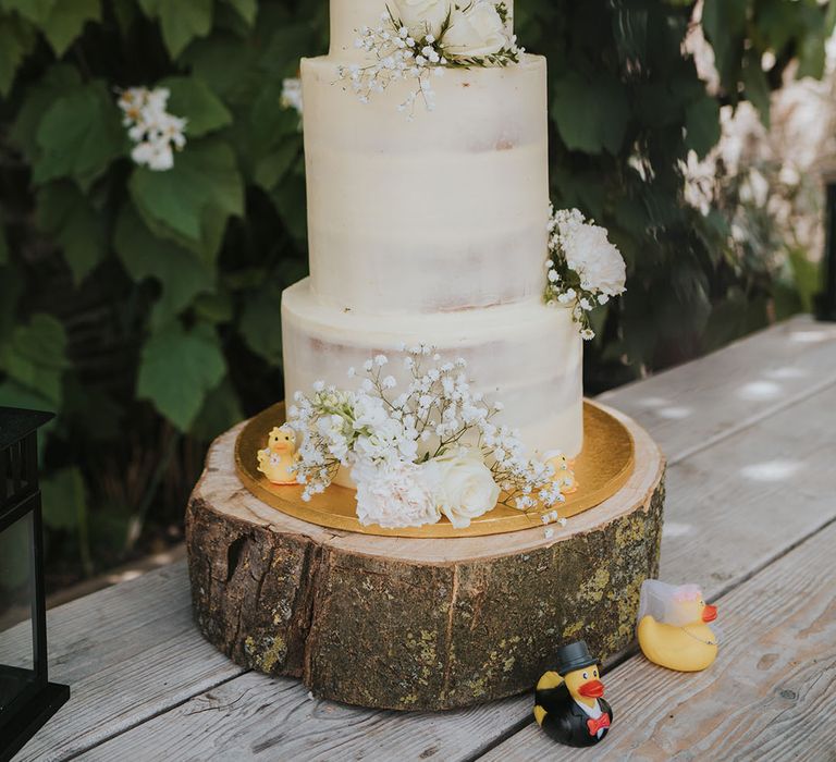 Three tier wedding cake with white icing decorated with white roses and gypsophila with bride and groom rubber ducks 