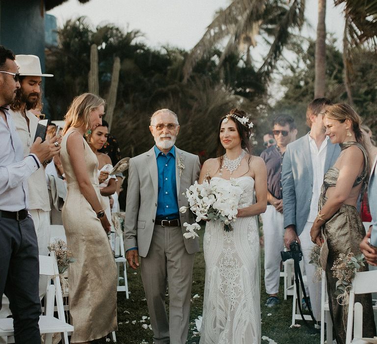 Father of the bride walks bride wearing a boho lace wedding dress with white orchid wedding bouquet down the aisle