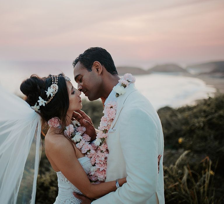 Bride and groom kiss during sunset portraits at Tigre Del Mar wedding with bride's veil floating in the air