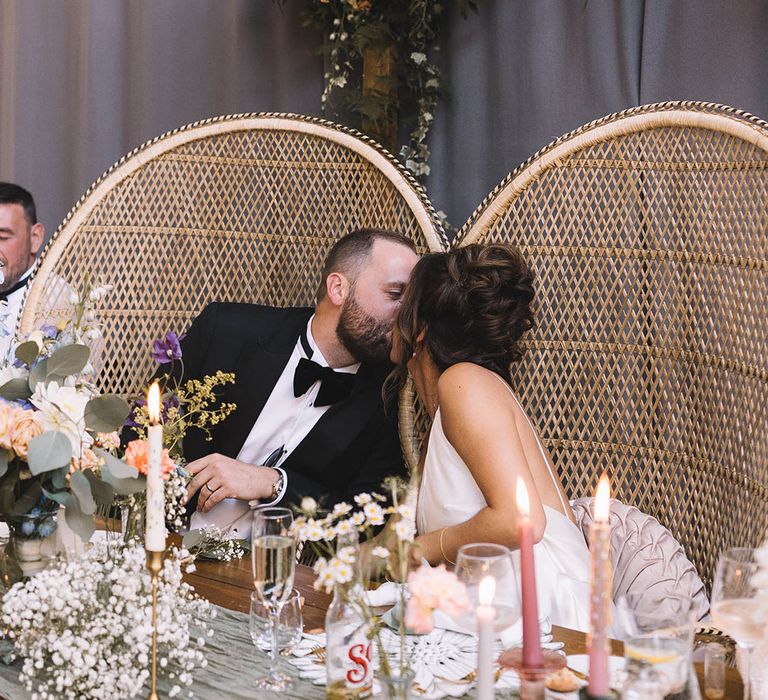 The bride and groom sit in peacock chairs and share a kiss at Bowers Mill Yorkshire wedding 