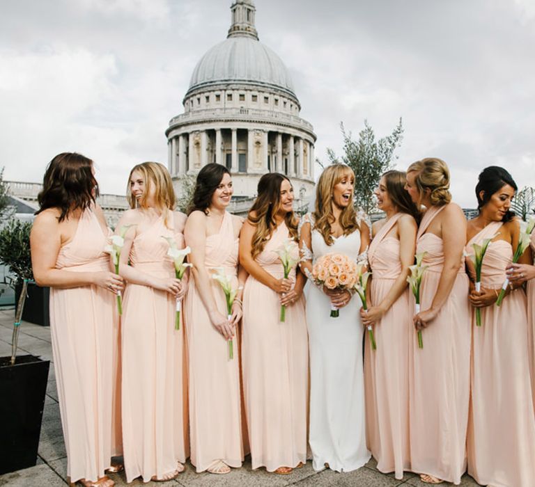 Bridal party in peach one shoulder bridesmaid dresses with the bride at city wedding 