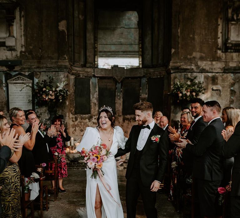 Bride wearing front slit puff sleeve wedding dress with groom in black tux walking back down the aisle 