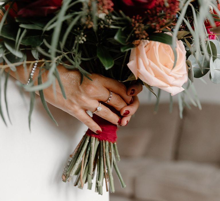 Bride wearing round diamond engagement ring holding rose wedding bouquet 