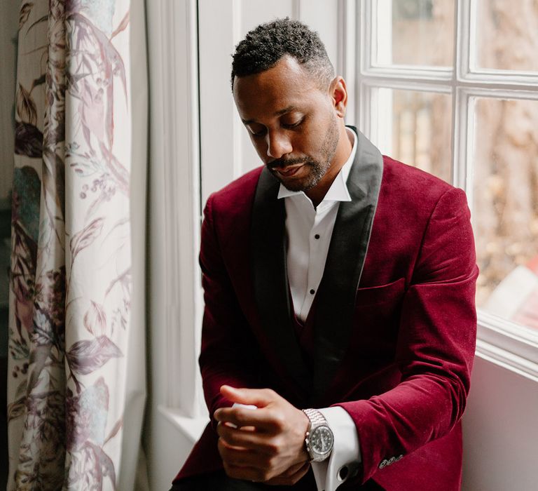 The groom gets ready for the wedding by putting on cufflinks wearing a red velvet suit jacket 