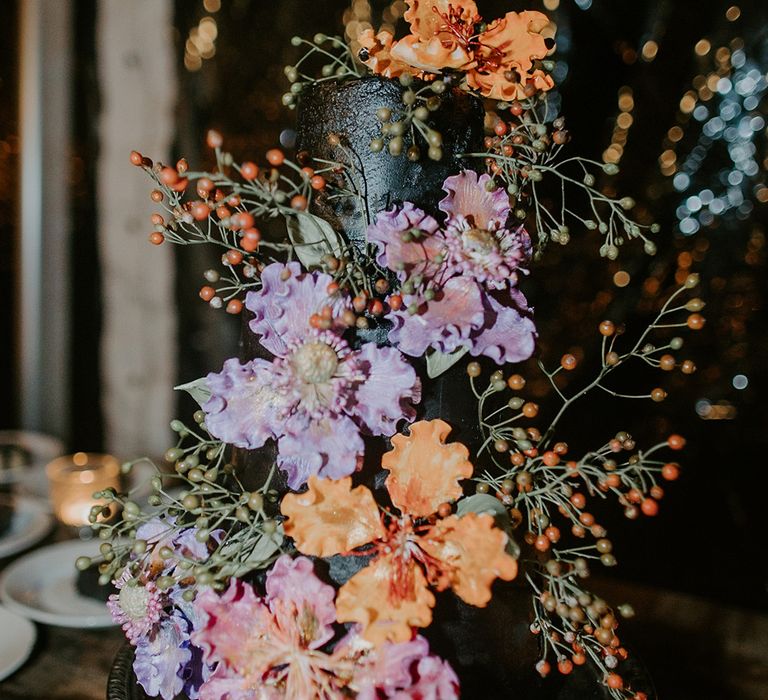 Three tier black iced wedding cake with purple and orange flower decorations 