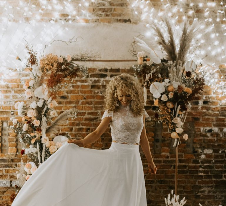 Curly haired bride wears lace bridal separates with fitted crop top as she holds silk white skirt beside her by Sarah Taylor Photography