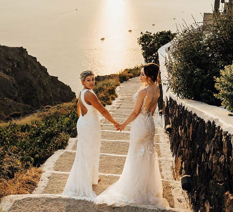 Two brides in boho lace wedding dresses walking during golden hour at their Santorini destination wedding in Greece 