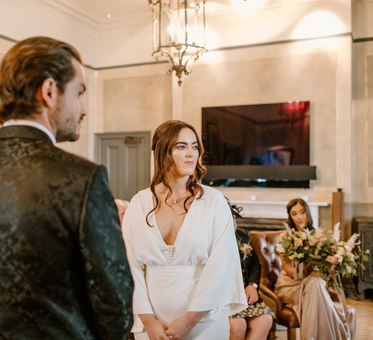 Bride and groom saying vows with bridesmaid in the background hol