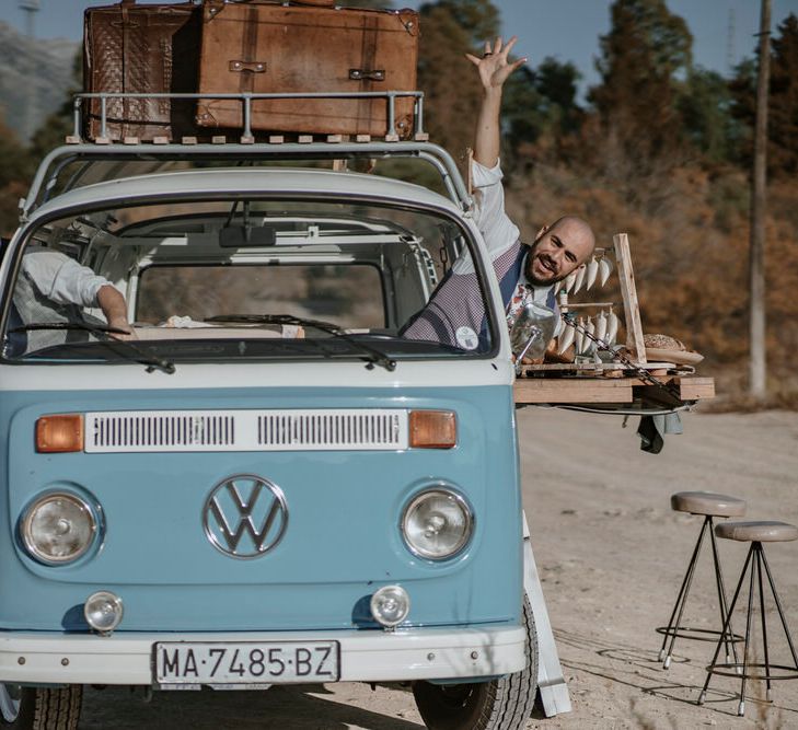 The grooms pose happily in the vintage blue camper van