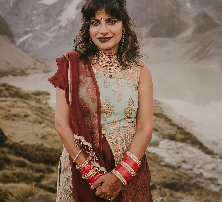 The bride wearing a beautiful traditional Indian wedding outfit in maroon, baby blue and gold.