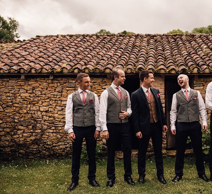 Groom in a navy suit with brown waistcoat and pink tie laughing with his groomsmen in black suits with grey waistcoats and pink ties | Samuel Docker 