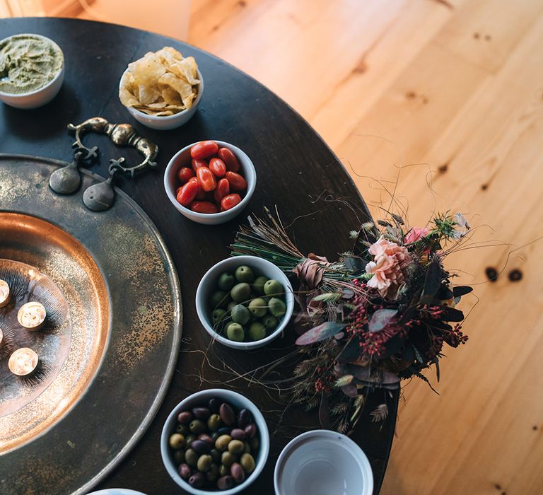 A table with lots of small bowls containing olives, tomatoes, crisps and other snack foods