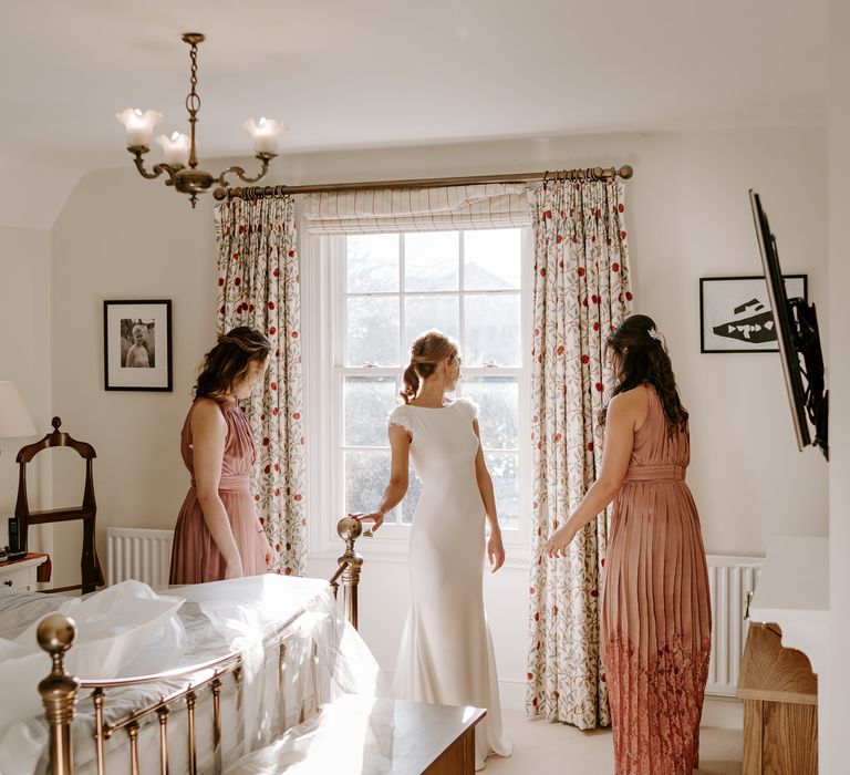 Wedding morning bridal preparations with bridesmaids in dusky pink pleated dresses with lace and halter neck design. 