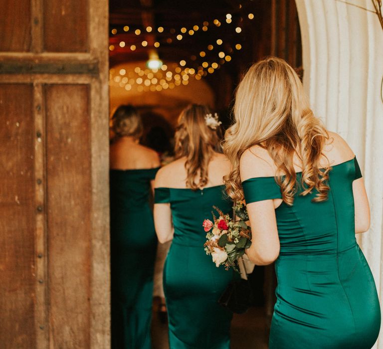 White bridesmaids with long blonde curly hair in off the shoulder dark green dresses walking into the church 